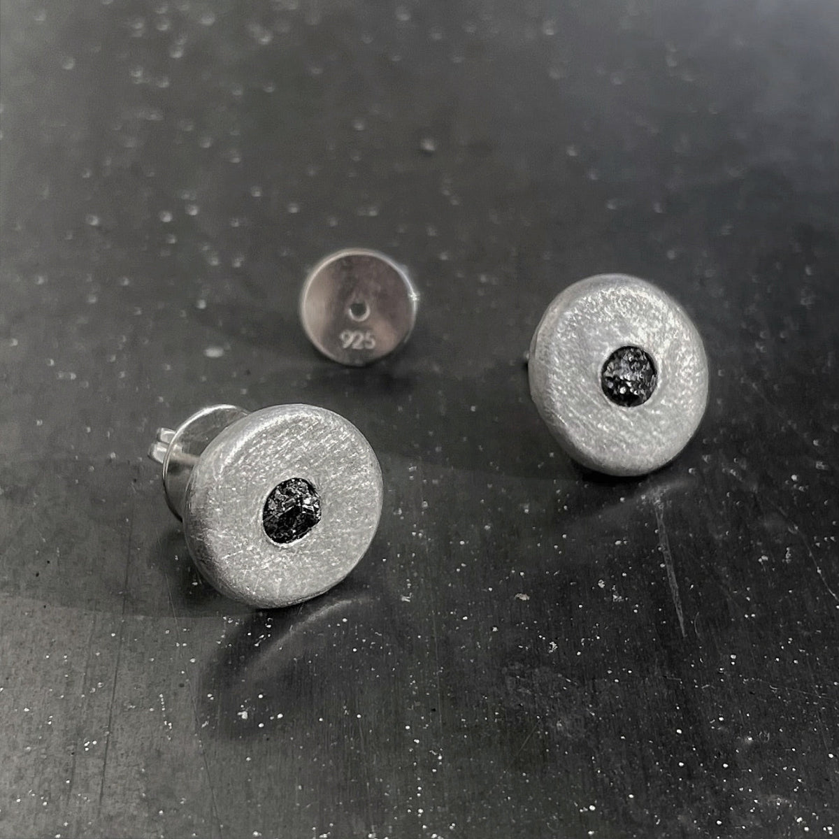Silver stud earrings with black gemstones on a dark textured surface