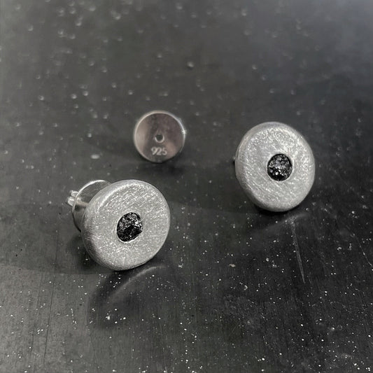 Silver stud earrings with black gemstones on a dark textured surface