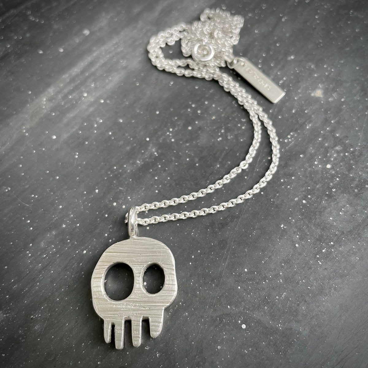 Silver skull pendant necklace on a dark textured surface