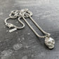 Silver necklace with a skull pendant on a textured gray surface