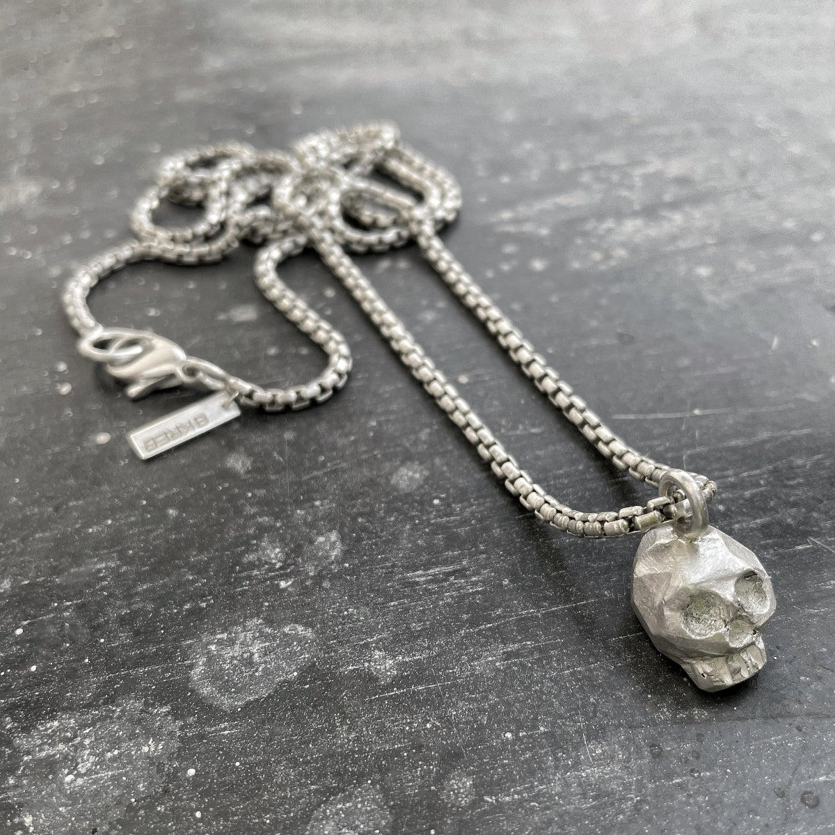 Silver necklace with a skull pendant on a textured gray surface